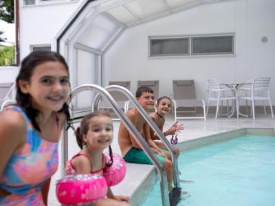 Lächelnde Kinder im Pool mit rosa Schwimmflügeln.