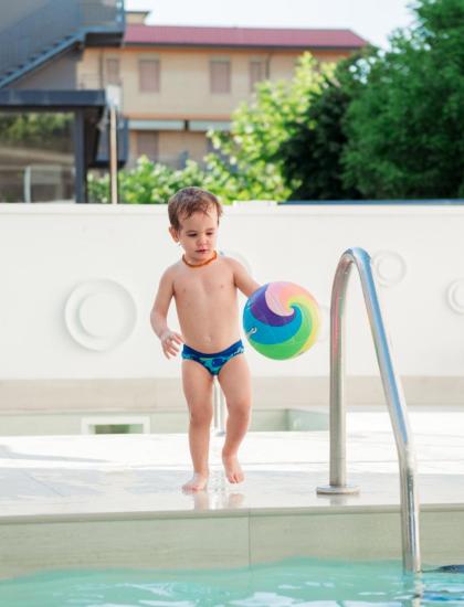 Kind mit buntem Ball am Pool.