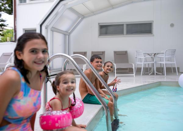 Lächelnde Kinder im Pool mit rosa Schwimmflügeln.