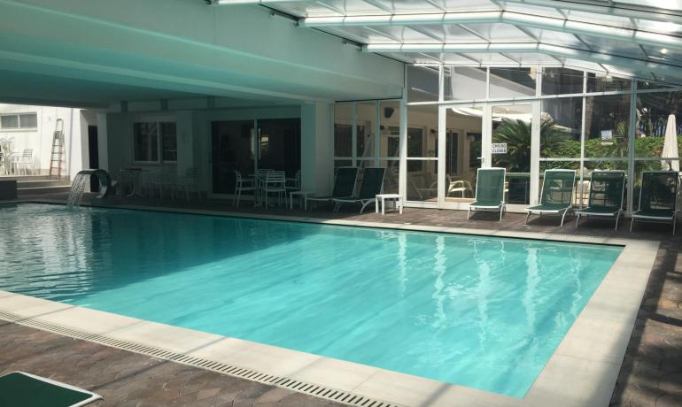 Piscina coperta con lettini verdi e cascata d'acqua.