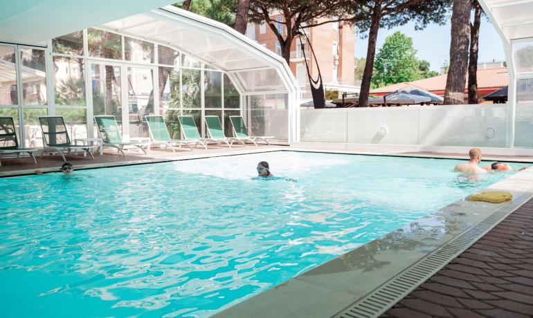 Piscine intérieure avec nageurs et chaises longues vertes.