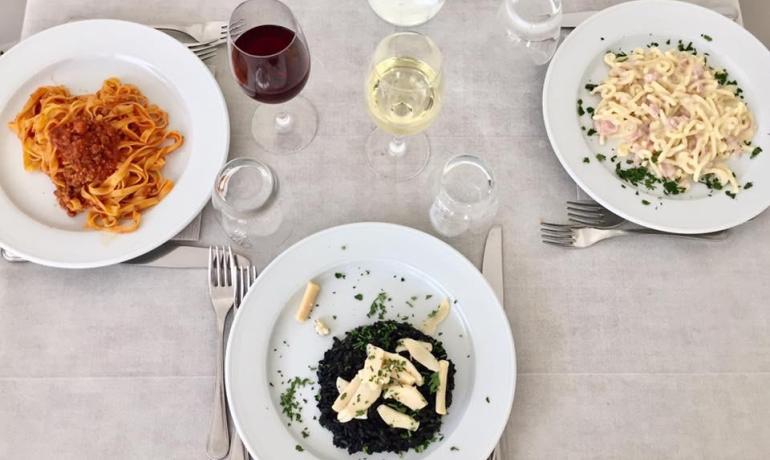 Tre piatti di pasta con vino e acqua su tavola apparecchiata.