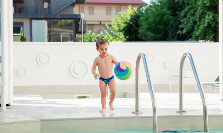 Bambino con palla colorata vicino alla piscina.