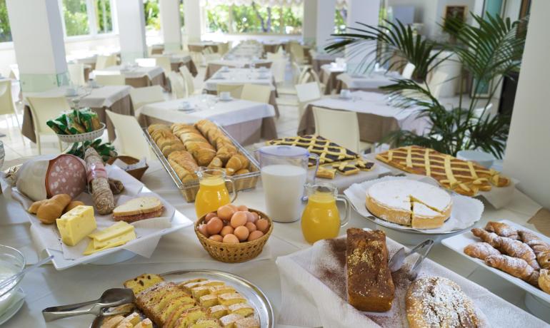 Buffet colazione con dolci, pane, salumi, formaggi, succhi e uova.