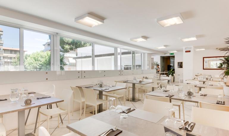 Ristorante moderno con arredi bianchi e tavoli apparecchiati.