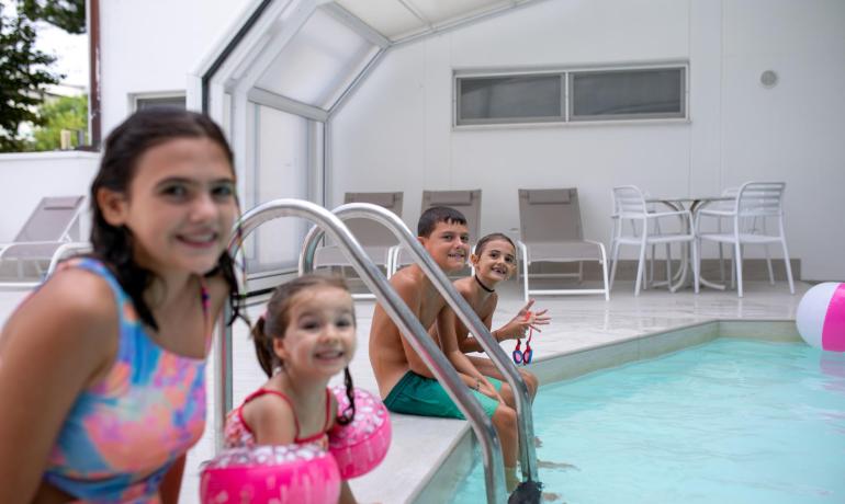 Bambini sorridenti in piscina con braccioli rosa.