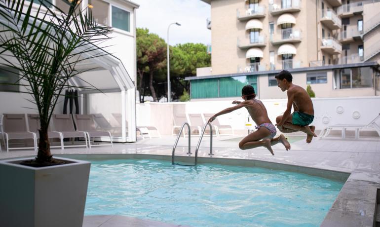 Due bambini saltano in piscina in un ambiente urbano.