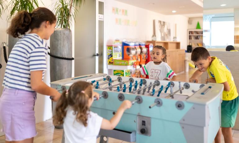 Bambini giocano a biliardino in una sala giochi luminosa.