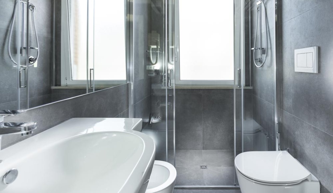 Bagno moderno con doccia in vetro, lavabo bianco e pareti grigie.