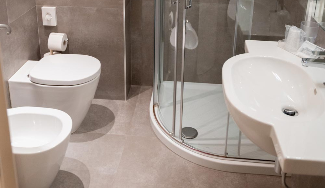 Bagno moderno con doccia angolare, bidet e lavandino su piastrelle grigie.