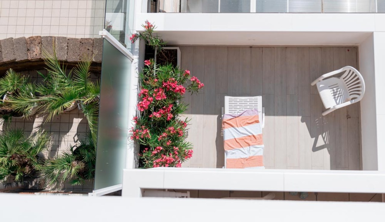 Terrazza soleggiata con sdraio, sedia bianca e fiori rosa.