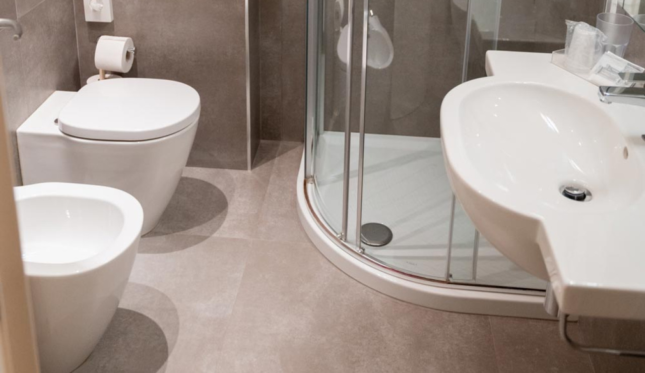 Bagno moderno con doccia, lavabo, WC e bidet, piastrelle grigie.