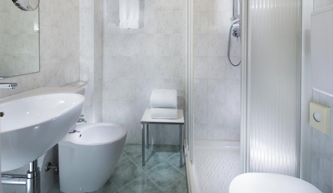 Bagno moderno con doccia, lavabo, bidet e asciugamani su tavolino.