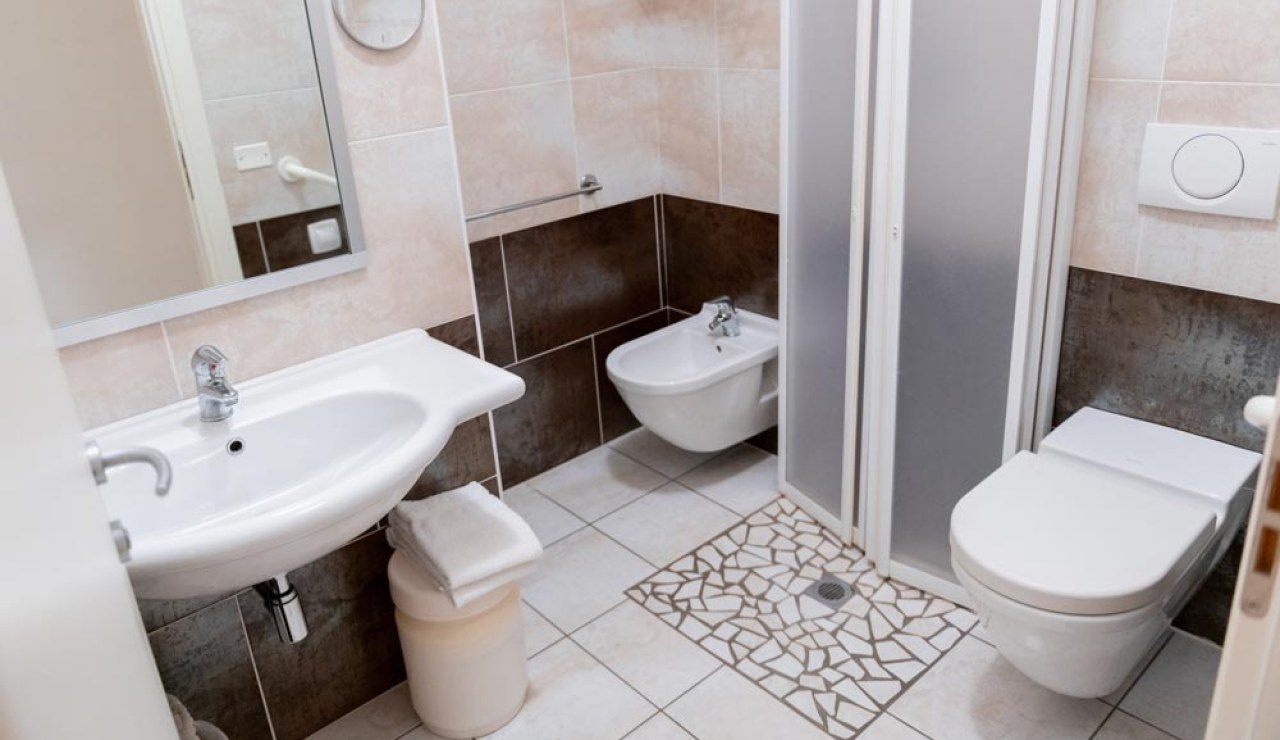 Bagno moderno con doccia, lavabo, bidet e WC, piastrelle chiare e scure.