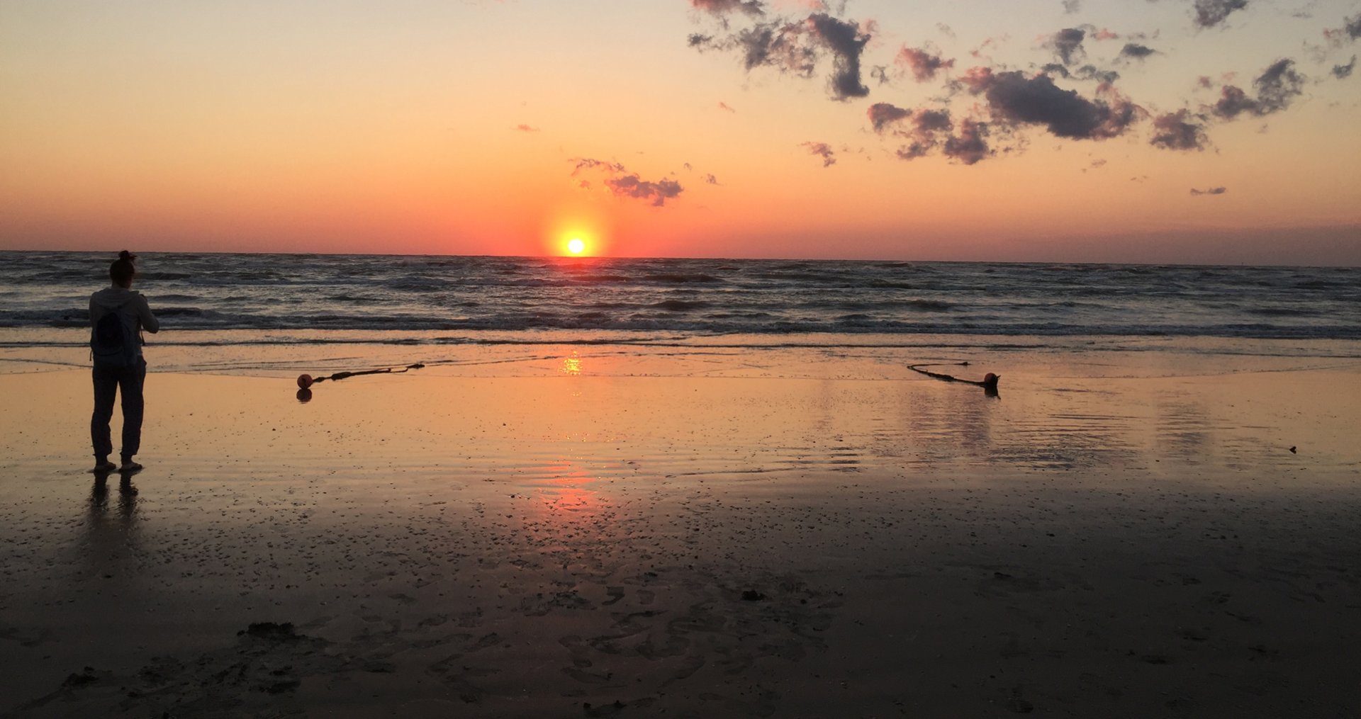 Persona guarda il tramonto sulla spiaggia, con il sole che si riflette sull'acqua.