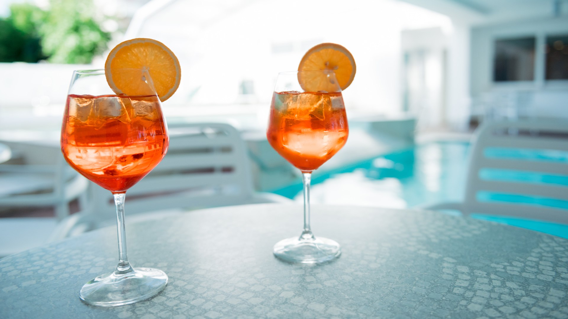 Due bicchieri di Aperol Spritz con fette d'arancia, vicino a una piscina.