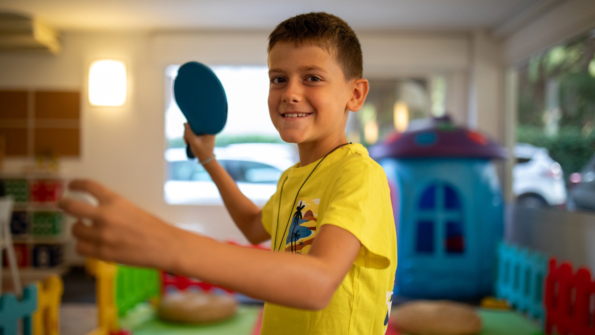 Bambini sorridenti sdraiati su tappeti colorati, facendo il segno di pace con le mani.