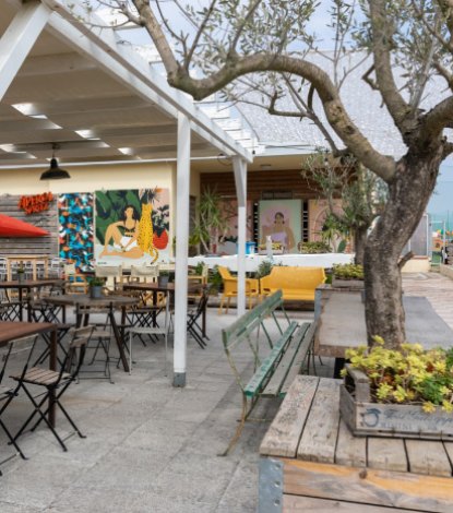 Terrazza con tavoli e sedie, decorata con murales colorati e piante.