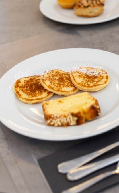 Piatto con pancake e fetta di dolce spolverati di zucchero a velo.