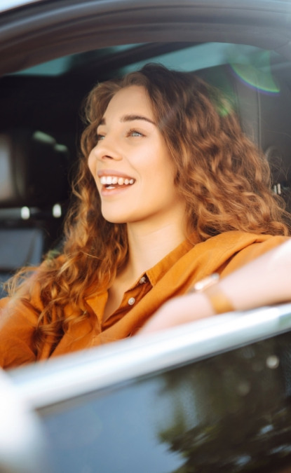 Giovane donna sorridente con capelli ricci, seduta in macchina, felice e rilassata.