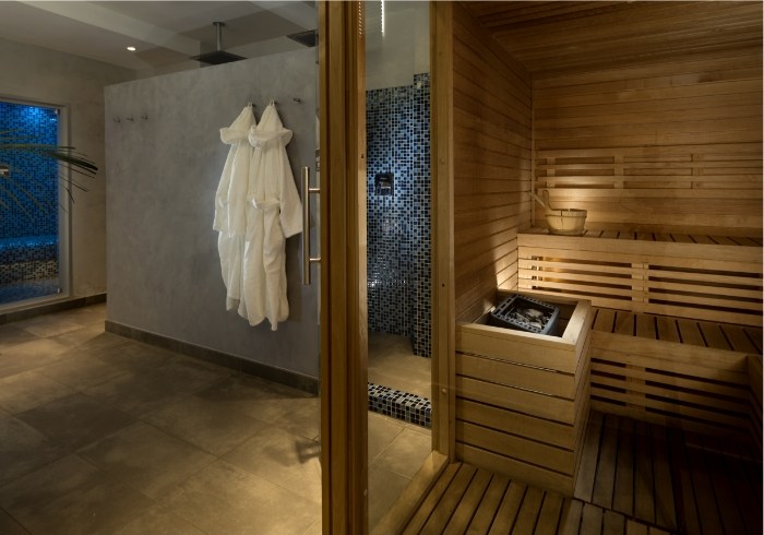 Spa con sauna in legno, accappatoi appesi e doccia con mosaico blu.