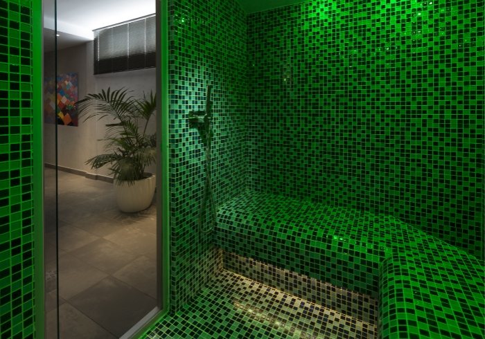 Bagno turco moderno con mosaico verde, illuminazione soffusa e piante decorative.