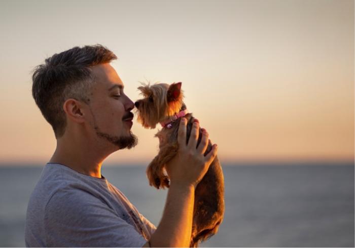 Uomo abbraccia un cane piccolo al tramonto sulla spiaggia.