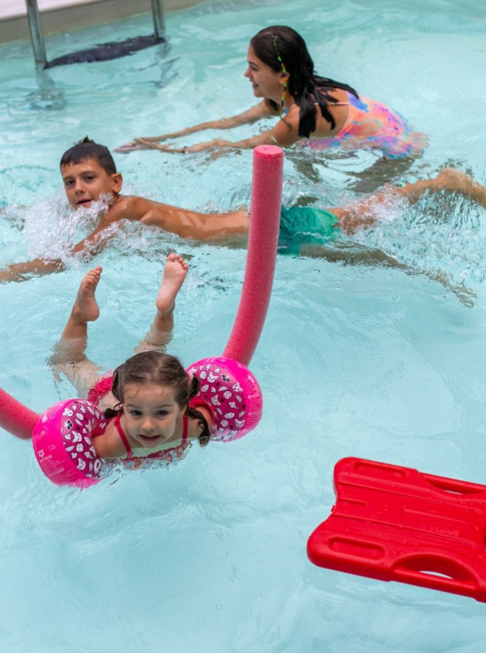 Bambini giocano in piscina con braccioli e noodle galleggiante.