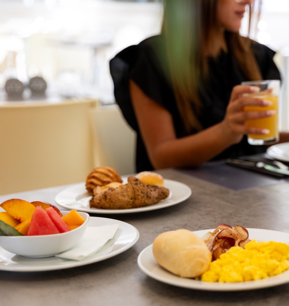 Colazione con frutta fresca, uova strapazzate, pancetta, pane e succo d'arancia.