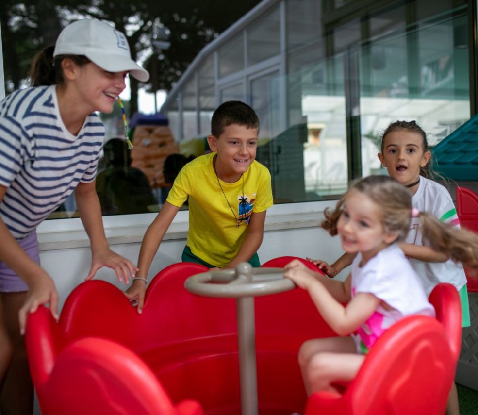 Bambini giocano felici su una giostra rossa in un ambiente chiuso.