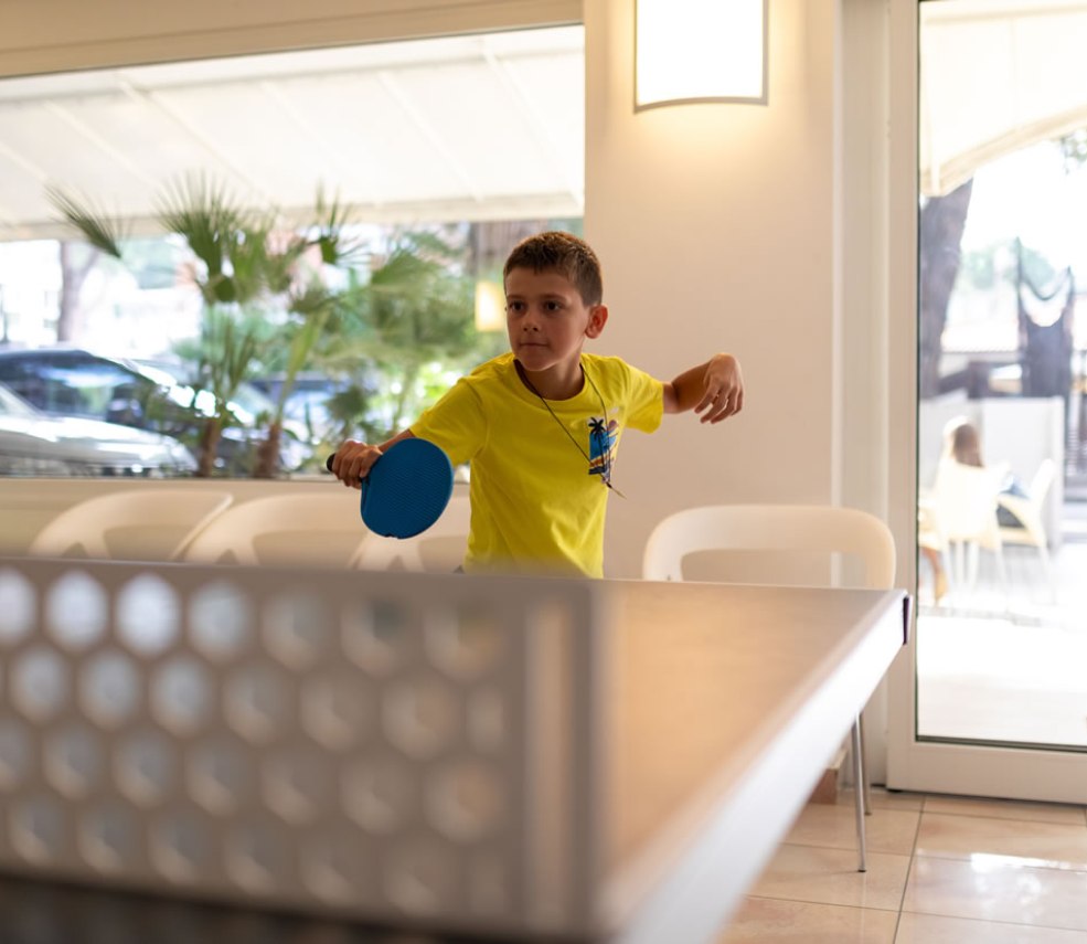 Bambino gioca a ping pong in una stanza luminosa con finestre grandi.