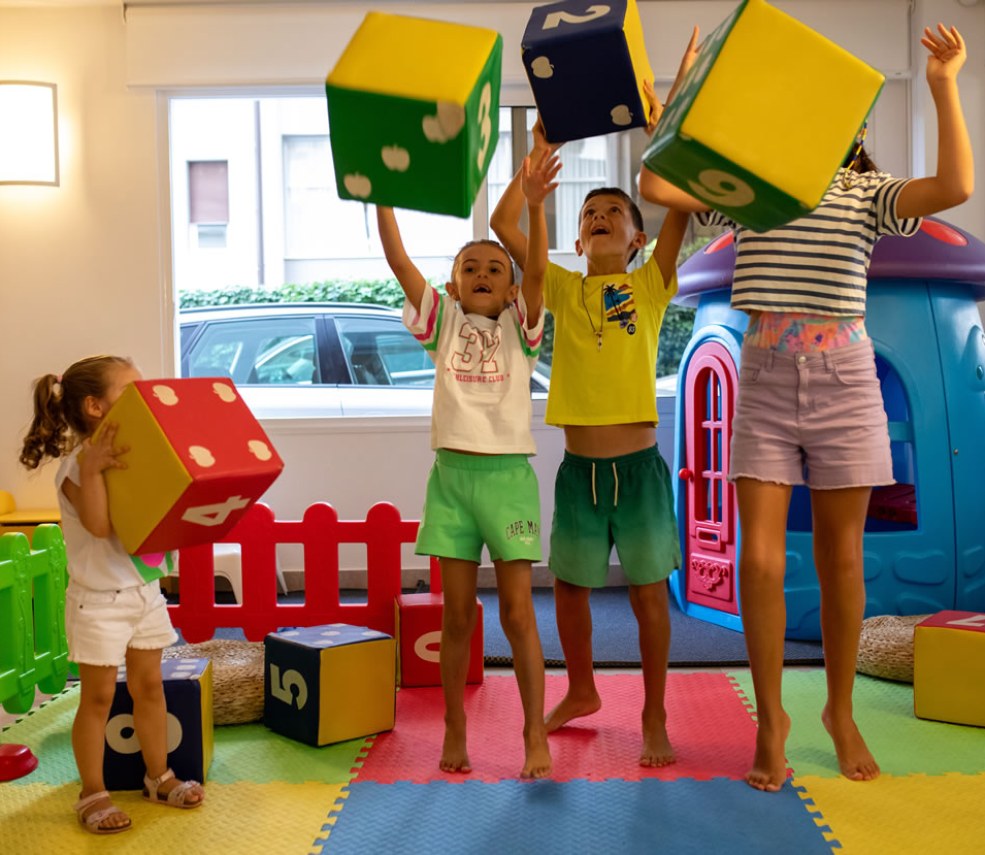 Bambini giocano con cubi colorati in una stanza piena di giochi.