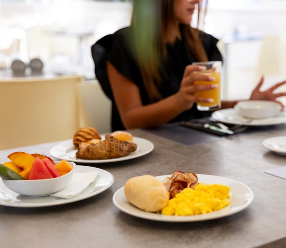 Colazione con uova strapazzate, frutta fresca e succo d'arancia in un ambiente luminoso.