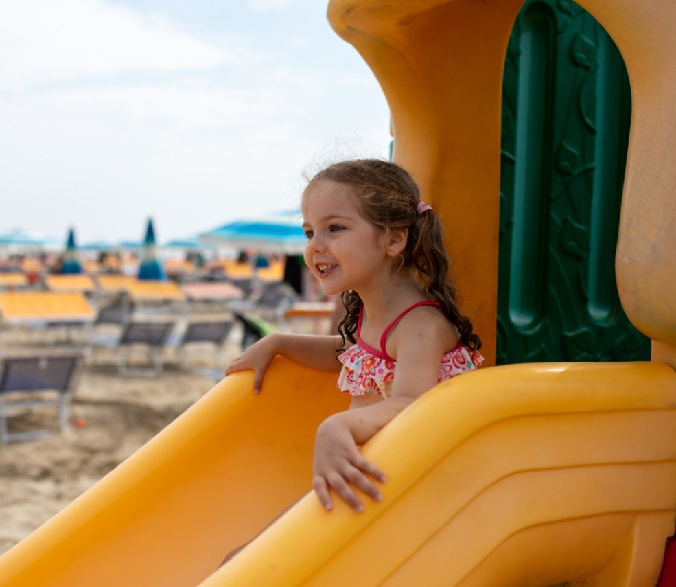 Bambina sorridente su uno scivolo al parco giochi in spiaggia.